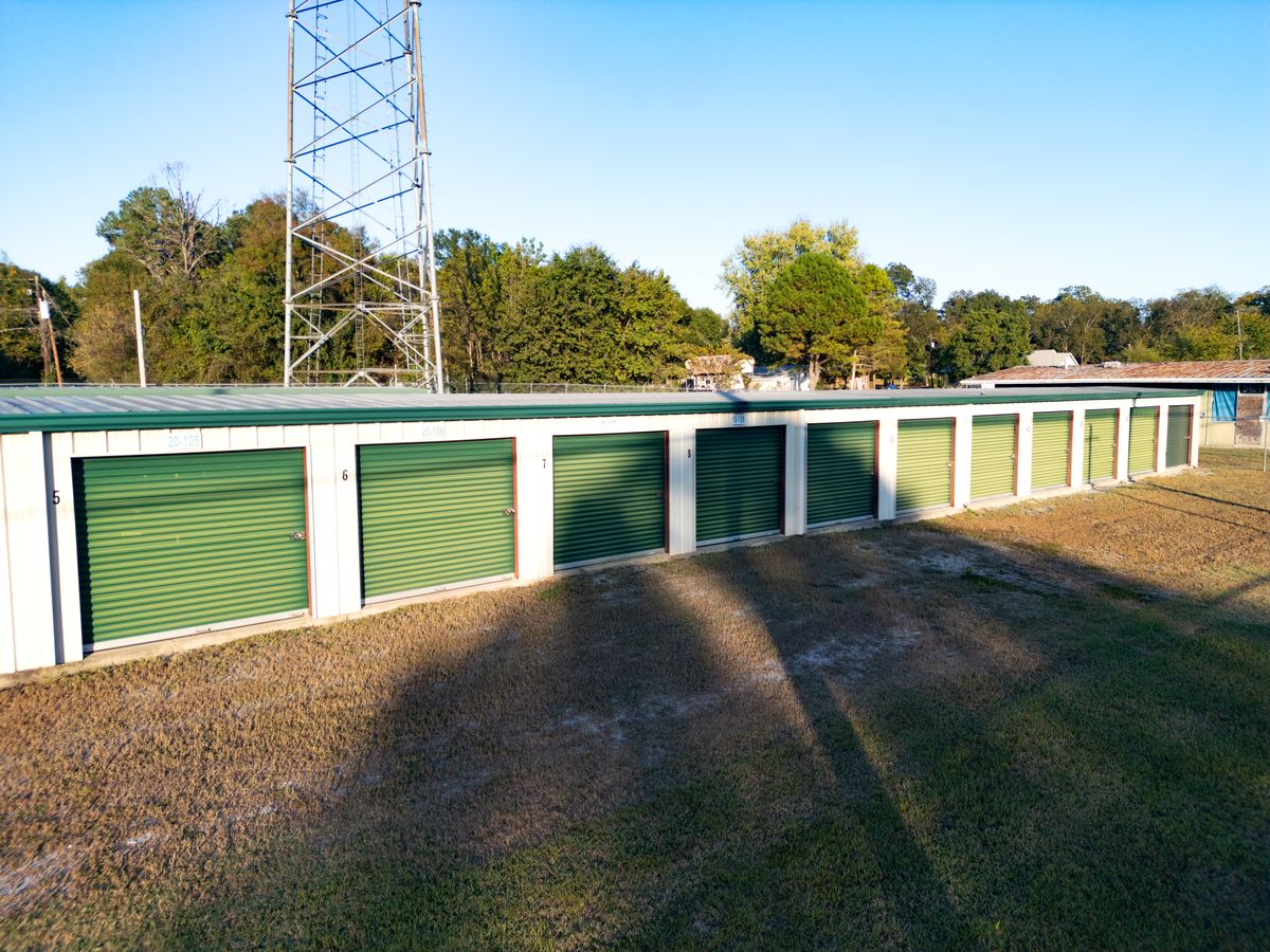 A row of Store Base storage units with green roll-up doors under a clear sky